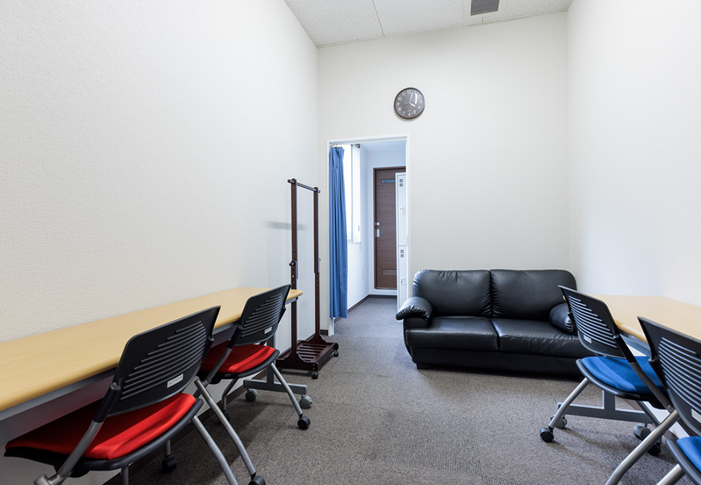部屋の内装写真。壁に机1つに椅子が2つの組み合わせが2セットと2人がけのソファが1つ置かれた部屋。